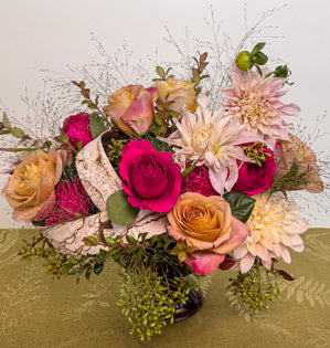 A horizontal design in a brown compote, full of Symbol and Darcy garden roses, cafe au lait dahlias, red huckleberry, seeded eucalyptus, and fountain grass, accented with a barked ribbon.