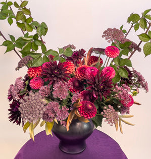A luxurious black cauldron overflowing with a variety dahlias, chocolate Queen Anne's lace, peony foliage, eupatorium, and blackberry vines.