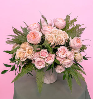A simple white vase overflowing with lush Juliet, Sahara Sensation and Wedding Rosever garden rose varieties, paired with Italian ruscus, oregonia, and umbrella fern. 