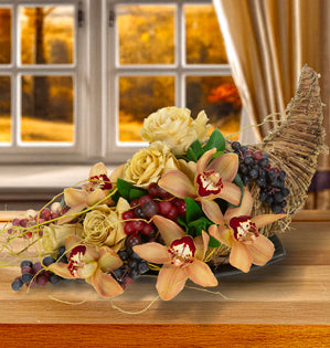 Mocha Mousse Cornucopia Centerpiece with soft beige roses, warm cymbidium orchids, and clusters of grapes.