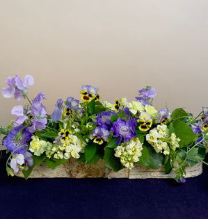 A trio of salal, ruscus, and galax sets the stage for soft yellow stock and mini carnations.