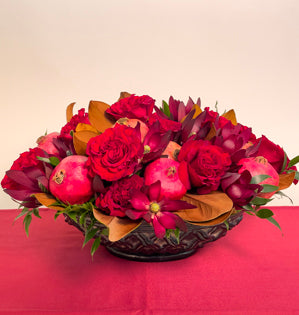 A luxurious oval centerpiece filled with Wanted garden roses, leucadendron, magnolia leaves, Italian ruscus, and vibrant pomegranates.