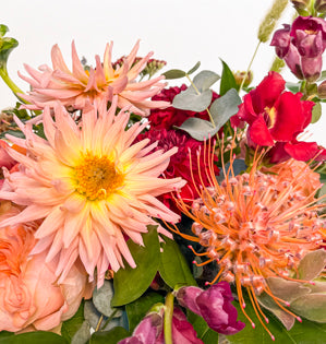 A close up image of dahlias and pin cushion protea surrounded by snap dragons, garden roses, and silver dollar eucalyptus