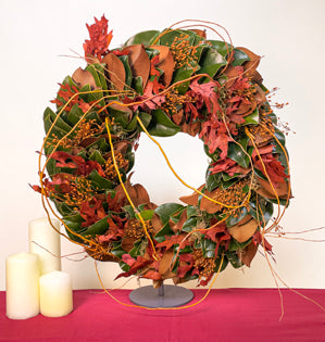 A large wreath comprised of magnolia leaves, with sphagnum moss, tinted preserved oak leaves, dried grasses, and scarlet curly willow extending from the base.