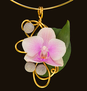 A gold pendant-style necklace features a soft pink miniature Phalaenopsis orchid.