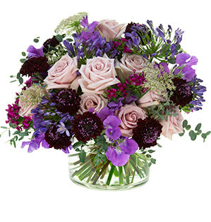 A hand-tied bouquet in purple and dusty pink colors mixes scabiosa, sweet peas, quick sand roses and Queen Anne's lace.