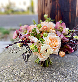A spiral hand tied wedding bouquet features Princess Maya and Golden Mustard roses, hellebores, strawflower, butterfly ranunculus, and agonis.