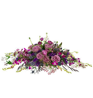 A long horizontal centerpiece in lovely tones of magenta and violet is comprised of Tiara roses, dendrobium orchids, ranunculus, agonis, eryngium, jasmine vine, and snapdragons.