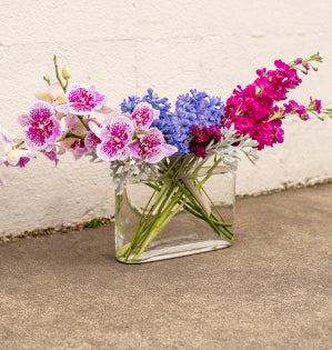 A horizontal design mixes  luxurious violet Phalaenopsis orchids, hyacinth, and scabiosa for a contemporary style.