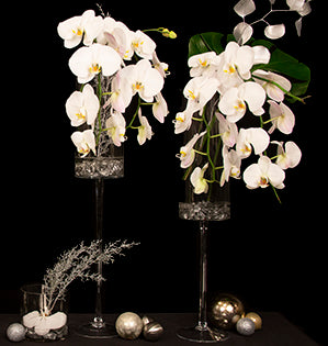 Stunning white Phalaenopsis orchids, metallic eucalyptus and glittered evergreen branches are featured in a collection of elevated containers.