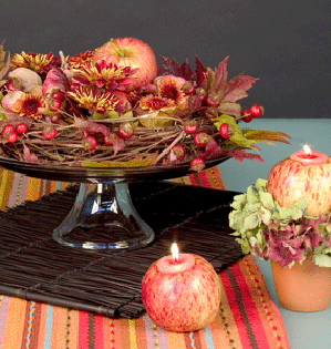 A festive autumn centerpiece uses a grape vine wreath as a base, and combines rose hips, apples, nuts, autumn chrysanthemums, and maple leaves on a lovely pedestal cake plate.