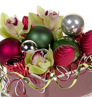 A holiday floral design mixes cymbidium orchid blooms with shiny Christmas ornaments and flat wire twisted into curlicues for a sparkling effect.