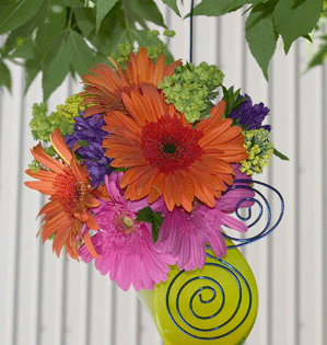 A colorful party vase decorated with aluminum wire and filled with summer flowers and foliage hangs from a tree for a unique and stylish display.
