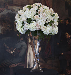 A dramatic, long lasting, stately and elegant (as well as mechanically sound) tall wedding table centerpiece is filled with hydrangeas, roses, ruscus and plumosa.