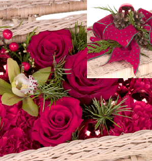 A festive Christmas flower basket mixes roses, carnations, berries, evergreens, glass balls, and one miniature cymbidium orchid, then it is finished with elegant ribbon.