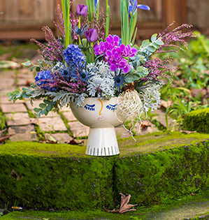 This beautiful spring floral design features paperwhites, irises, tulips, hyacinths, miniature Phalaenopsis orchids, dusty miller, acacia, eryngium, chloris magenta, and limonium in a unique head vase.