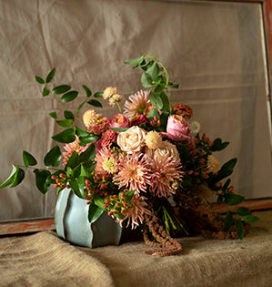 A spiral hand-tied bouquet combines dahlias, zinnias, scabiosa, and hanging amaranthus, in lush shades of peach.