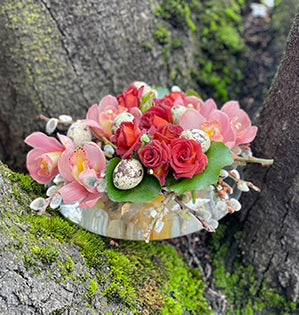 A small nested arrangement in red and pink mixes Cappuccino spray roses, miniature cymbidium orchids, pussy willow, galax leaves, and quail eggs. 