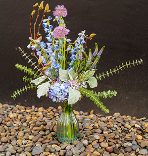 A big and bold vase arrangement includes hydrangea, delphiniums, veronica, and long-stemmed allium in delicate periwinkle tones.