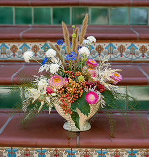 A compote floral design uses strawflowers, scabiosa, cornflowers, dried weeds, and various grasses for a free flowing look.