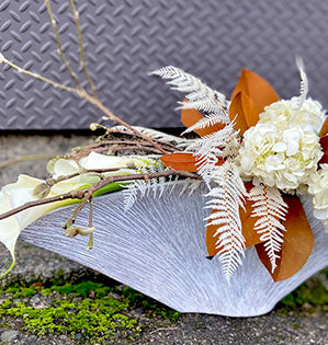 A beautiful floral design in a wind swept container mixes calla lilies, hydrangea, dried and preserved fern with magnolia leaves and branches.
