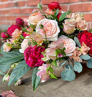 A lavish centerpiece mixes five varieties of garden roses accented with hellebores, two varieties of ranunculus, and peonies in dark pink, blush, and light pink colors.