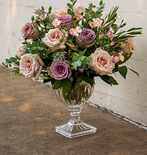 A hand-tied bouquet in a muted color palette mixes Quicksand and Amnesia garden roses, and miniature carnations with salal, olive, acacia, and fatsia leaves.