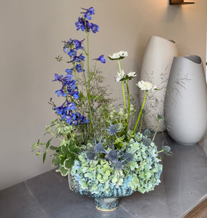 An arrangement with delphinium, hydrangea, eryngium, scabiosa, and delicate grasses.