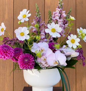 White vase with snapdragons, dahlias, phalaenopsis orchids, cosmos, and more.