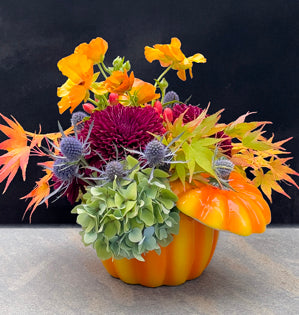 Chrysanthemums, hydrangea, eryngium, Japanese maple, and bright butterfly ranunculus in a ceramic pumpkin.