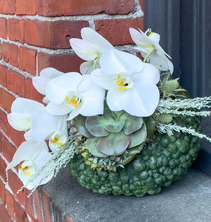 Decorative wreath with white flowers and greenery against a brick wall.