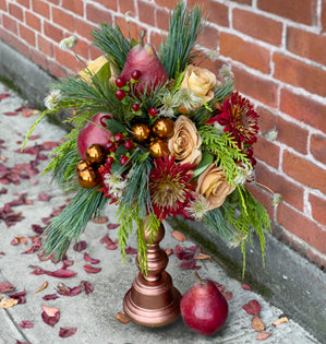 Decorative floral arrangement with pears on a pedestal against a brick wall.