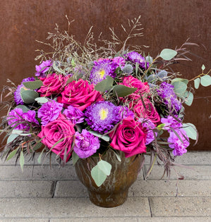 Blueberry roses, purple asters, miniature carnations, eryngium, eucalyptus, grasses, and agonis in a copper vase.