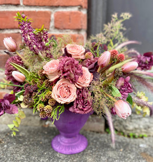 Floral arrangement in a purple vase against a brick wall.