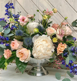 Floral arrangement with white and pink flowers in a silver vase on a wooden surface.