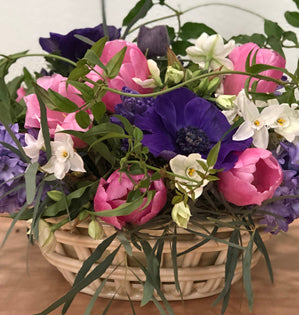 Basket of colorful flowers including pink, purple, and white on a wooden surface