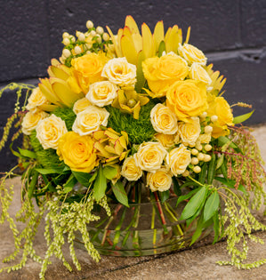 Bouquet of yellow and white flowers in a clear vase against a dark background