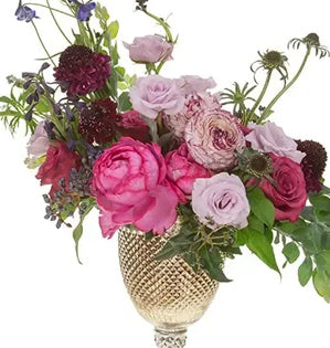 Floral arrangement with pink and purple flowers in a gold vase on a white background